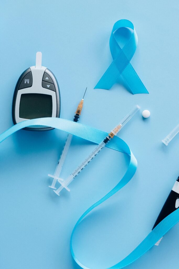 Flat lay of a glucose meter, syringe, and blue ribbon symbolizing diabetes awareness.