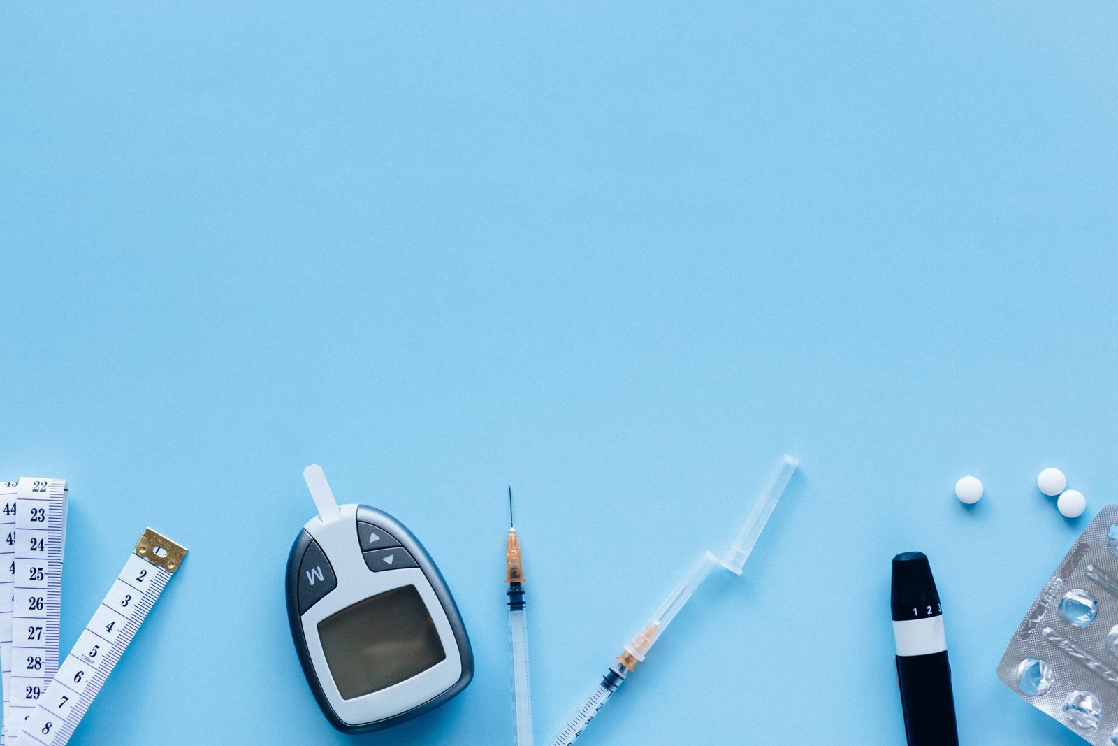 Flat lay of diabetes management tools including glucose meter, syringe, and pills on blue background.